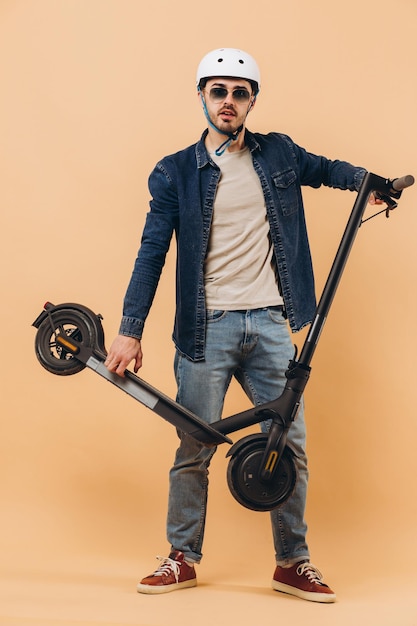 Hombre moderno con estilo en un casco con una foto de scooter electrónico en el estudio