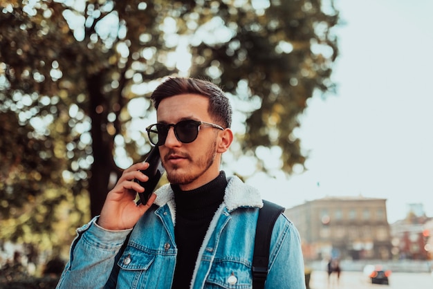 Hombre moderno con gafas de sol hablando por teléfono inteligente en la calle