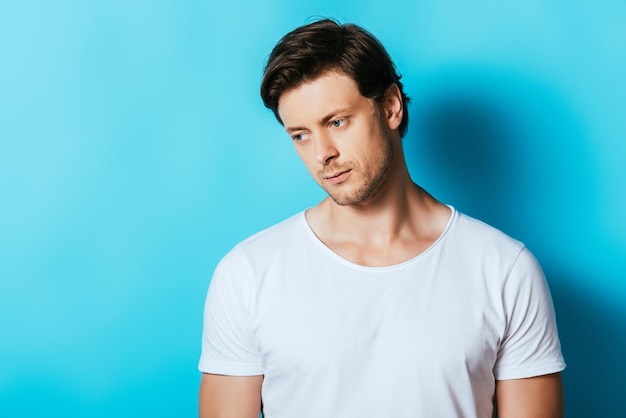 Hombre molesto con camiseta blanca mirando hacia otro lado con fondo azul