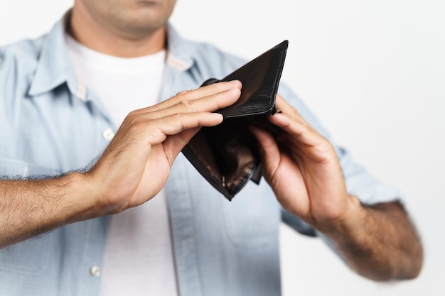 Foto hombre molesto sosteniendo boca abajo y mirando dentro de su billetera vacía sobre fondo blanco financiero