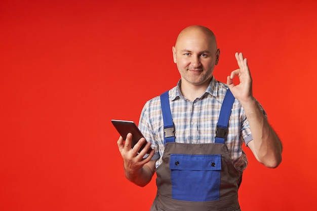 El hombre con un mono protector sostiene una tableta digital y muestra el signo OK