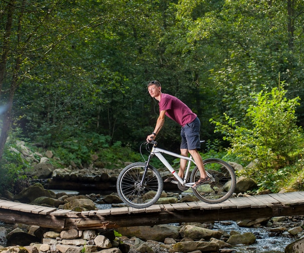 El hombre monta una bicicleta a través del puente de madera sobre un río