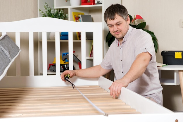 Un hombre monta una cama para niños mide la longitud con una cinta métrica