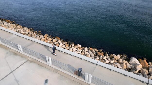 Un hombre monta una tabla larga en un paseo marítimo visto desde un dron