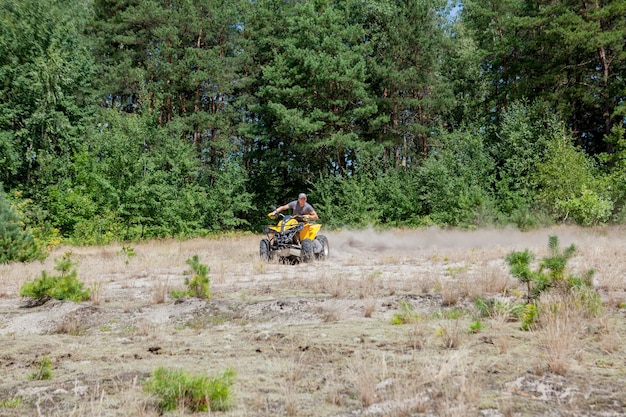 Hombre montado en un vehículo todo terreno quad ATV amarillo en un bosque arenoso.
