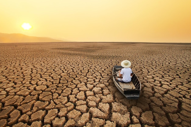 Hombre montando un bote de madera flotando en la tierra seca y agrietada