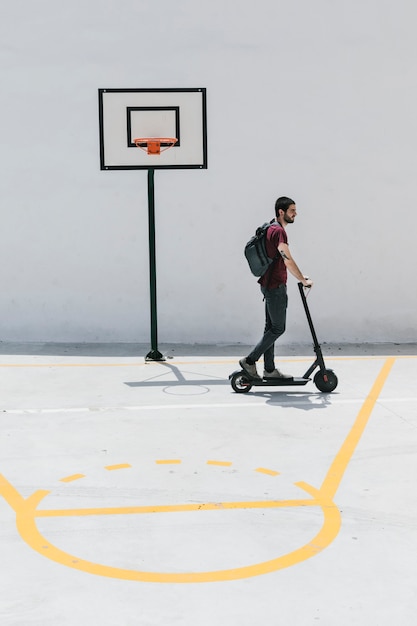 Hombre montando e-scooter en una cancha de baloncesto