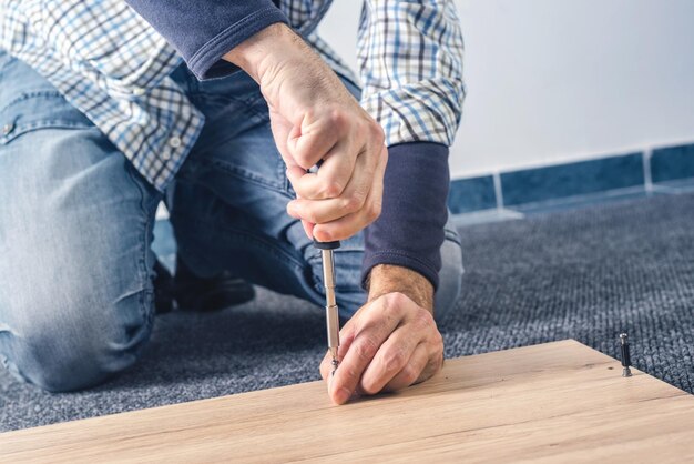 Hombre montando muebles en casa a mano con un destornillador