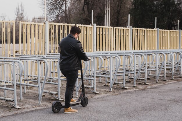 Hombre montando scooter ecléctico en el fondo de la valla