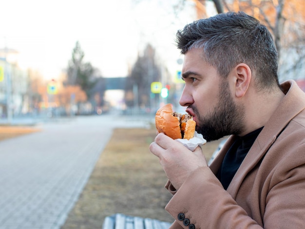 Hombre mordiendo una hamburguesa para llevar en la calle de cerca