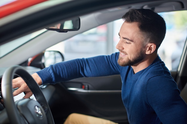 Hombre morena con barba en suéter azul sentado en coche nuevo.