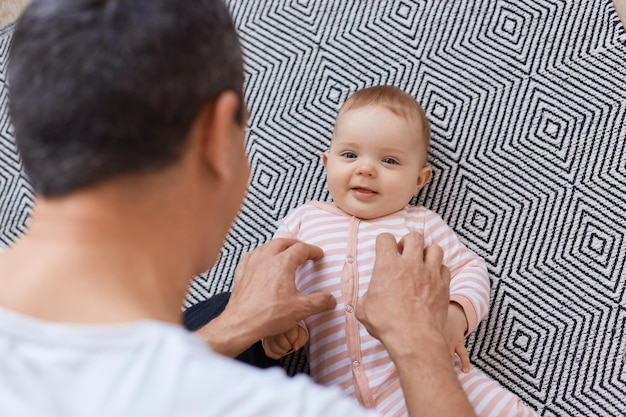 Hombre morena con camiseta blanca posando al revés a la cámara mientras juega con su pequeña hija en casa, tiempo feliz juntos en casa, familia y paternidad.