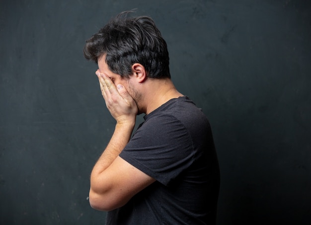 Hombre moreno cansado en camiseta negra en la pared oscura