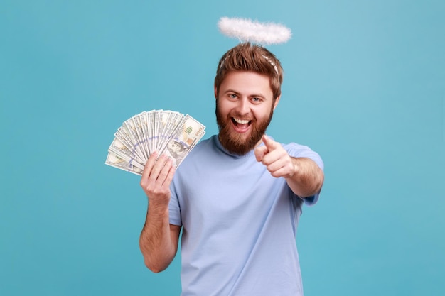 Hombre mostrando abanico de dinero sosteniendo billetes de dólar y apuntando a la cámara con el dedo índice