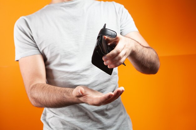 Hombre mostrando billetera vacía sobre fondo naranja