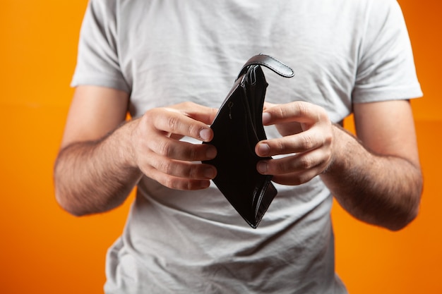 Foto hombre mostrando billetera vacía sobre fondo naranja