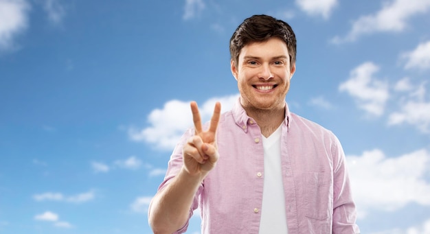 Foto hombre mostrando dos dedos o signo de paz sobre el cielo