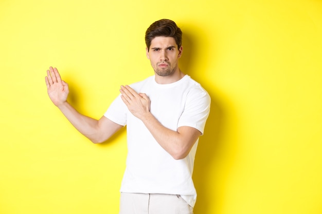 Hombre mostrando habilidades de kung-fu, movimiento ninja de artes marciales, de pie con camiseta blanca listo para luchar, de pie sobre fondo amarillo. Copia espacio