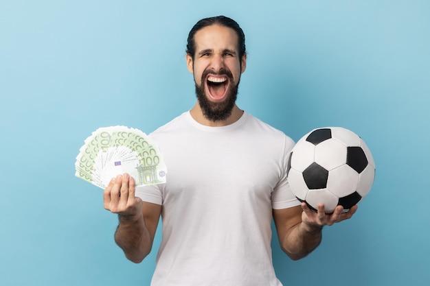 Hombre mostrando pelota de fútbol y diversión de billetes de cien euros ganando mucho dinero apostando por el deporte