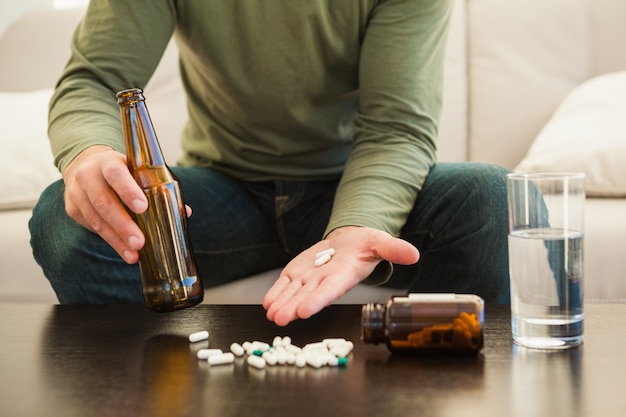 Hombre mostrando píldoras y sosteniendo la botella de cerveza