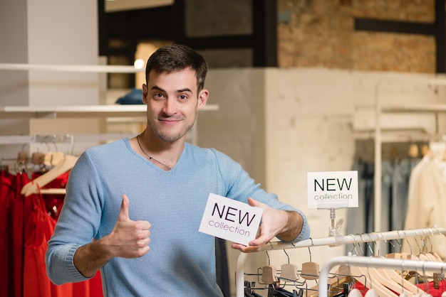 Foto hombre mostrando el pulgar hacia arriba y mantenga el cartel blanco con nuevas palabras de colección