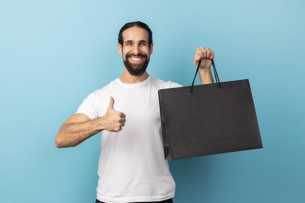 Hombre mostrando los pulgares hacia arriba sosteniendo una bolsa de compras complacido con buenas compras y recomendaciones de descuentos