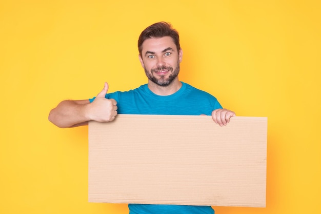 Hombre mostrando los pulgares hacia arriba sosteniendo un tablero en blanco promocional en el fondo del estudio un cartel en blanco con copyspace
