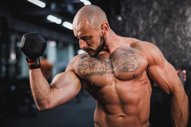 Foto hombre mostrando sus músculos mientras se entrena con pesas en el gimnasio