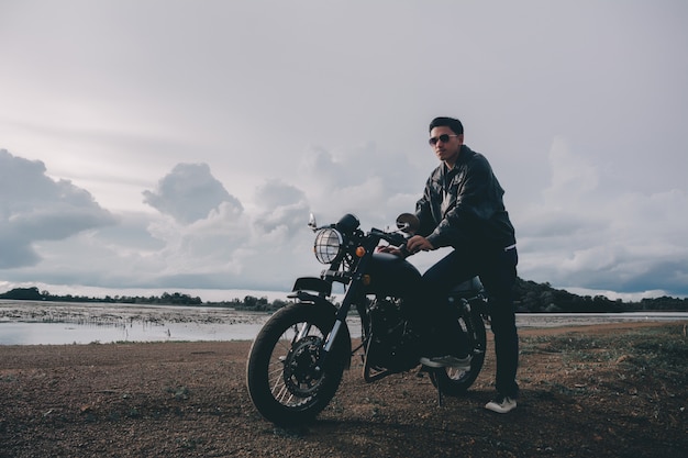 Hombre motero con su moto al lado del lago natural y hermoso.