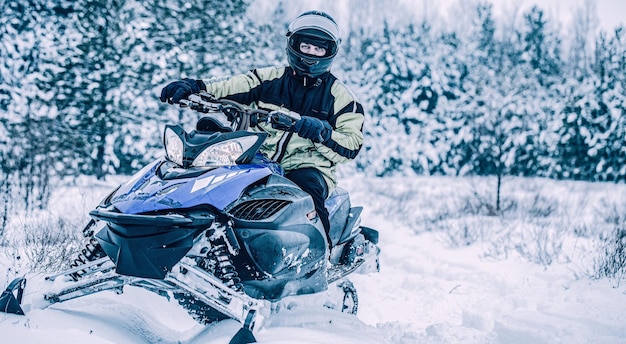 Hombre en moto de nieve en la montaña de invierno Conducción de motos de nieve Hombre conduciendo motos de nieve en un bosque nevado