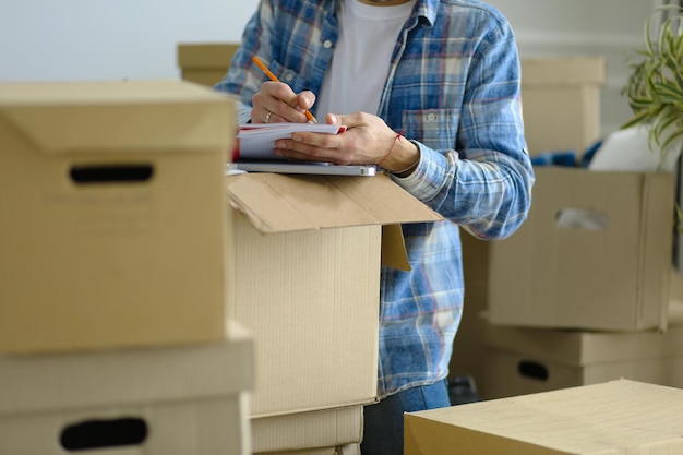 Un hombre en movimiento sentado en el suelo en un apartamento vacío Entre las cajas Comprobación de la lista de cosas