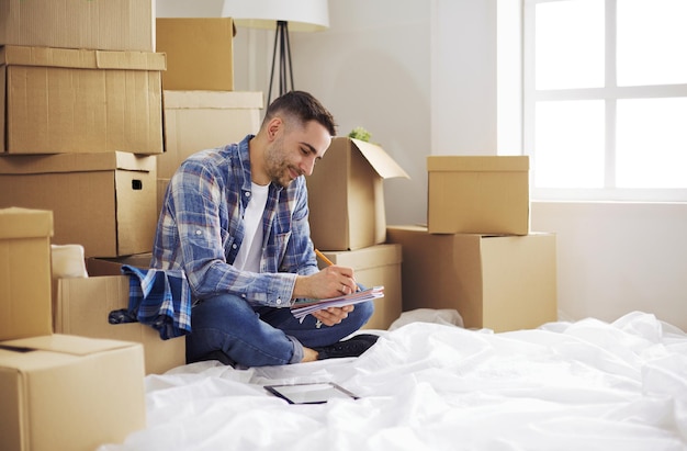 Un hombre en movimiento sentado en el suelo en un apartamento vacío Entre las cajas Comprobación de la lista de cosas