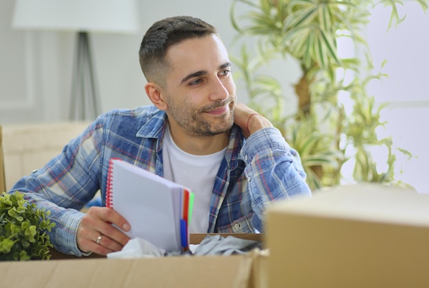 Un hombre en movimiento sentado en el suelo en un apartamento vacío Entre las cajas Comprobación de la lista de cosas