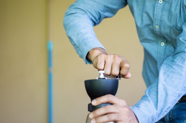 Un hombre muele los granos de café con una batidora de mano.