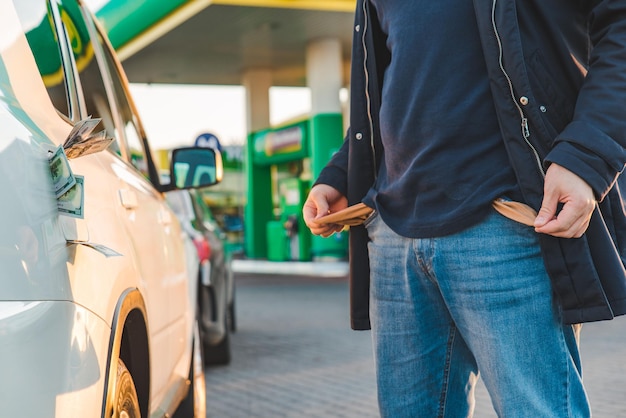 El hombre muestra el bolsillo vacío en la gasolinera. dinero en concepto de tanque de coche