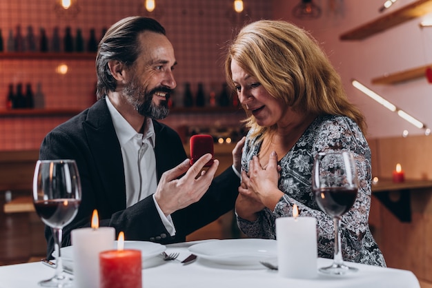 El hombre muestra una caja con un anillo de bodas a una mujer entusiasta durante la cena en un restaurante