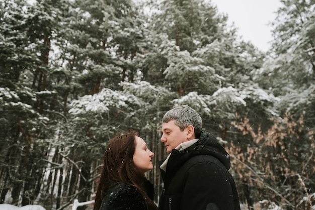 Hombre y mujer adultos en el fondo de un bosque de pinos cubiertos de nieve en invierno