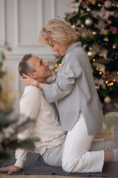 hombre y mujer adultos se sientan en el suelo cerca del árbol de navidad y se abrazan