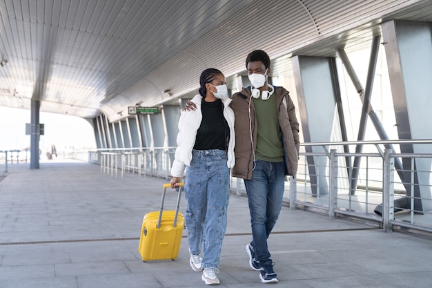 El hombre y la mujer africana caminan hacia la salida del avión fuera del aeropuerto con máscaras protectoras