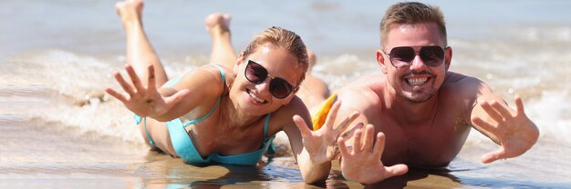 Hombre y mujer alegre en gafas de sol se encuentran en la arena mojada cerca del mar