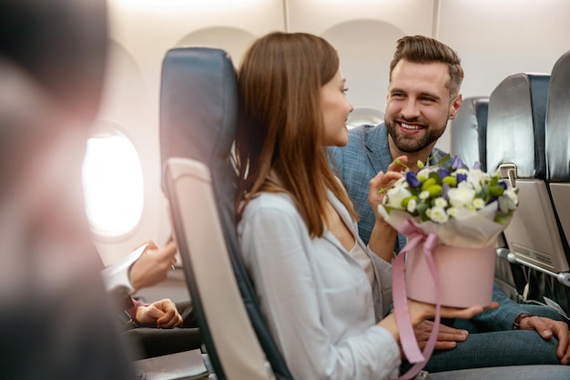 Hombre y mujer alegres con flores viajando en avión