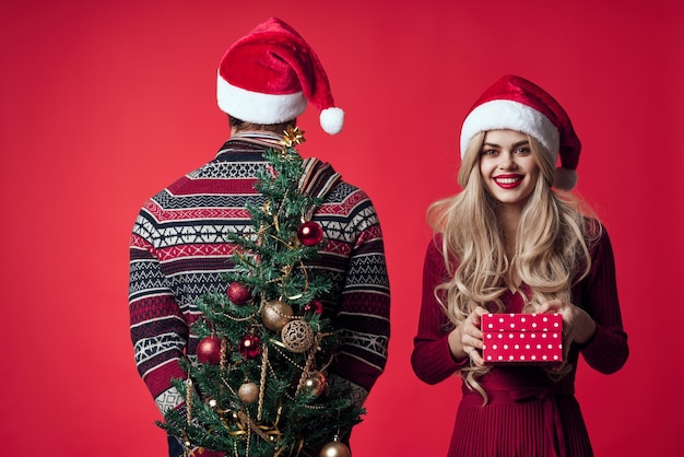 Hombre y mujer árbol de navidad juguetes regalos vacaciones fondo rojo