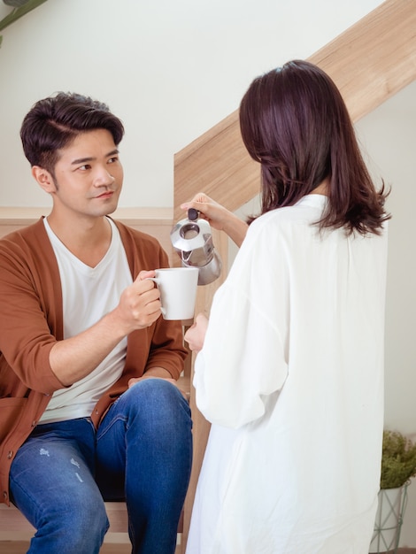 Hombre y mujer asiática joven disfrutan de pasar tiempo juntos en casa con una taza de café en las manos.