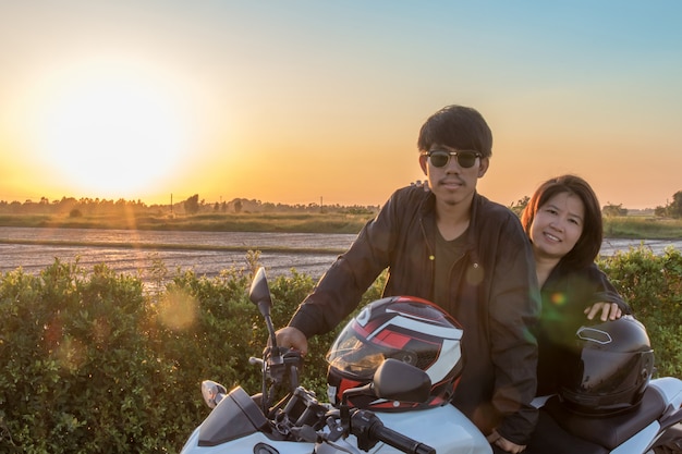 Hombre y mujer asiáticos con casco y usar y abrocharse antes de andar en bicicleta grande moto en la carretera por seguridad