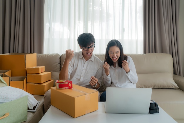 El hombre y la mujer asiáticos están vendiendo en línea a través de la computadora en casa y muy satisfechos cuando hay muchos de sus pedidos. PYME emprendedora de pequeñas empresas o concepto independiente