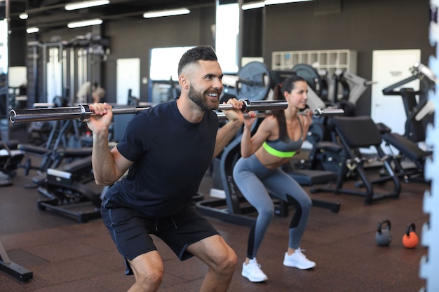 Hombre y mujer con barra flexionando los músculos en el gimnasio.