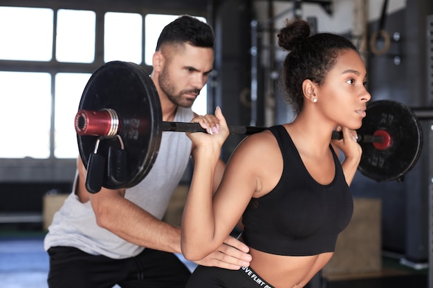 Hombre y mujer con barra flexionando los músculos en el gimnasio.