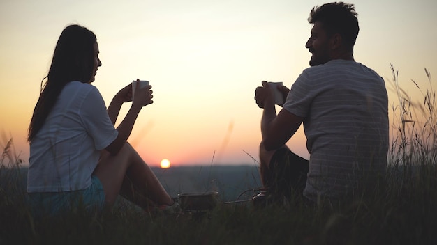 El hombre y la mujer bebiendo té en el hermoso fondo de la puesta de sol