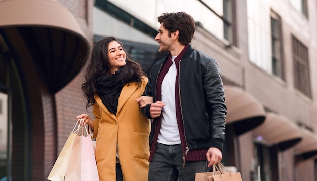 Un hombre y una mujer caminan por una calle concurrida con bolsas de compras en las manos