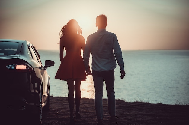 El hombre y la mujer caminando cerca del coche en la orilla del mar.